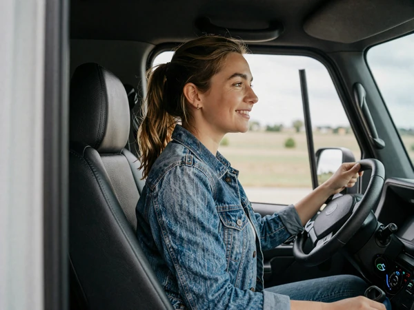 Young woman in a denim jacket sitting in a semi truck cab looking out the window, natural daylight, candid portrait for trucker dating